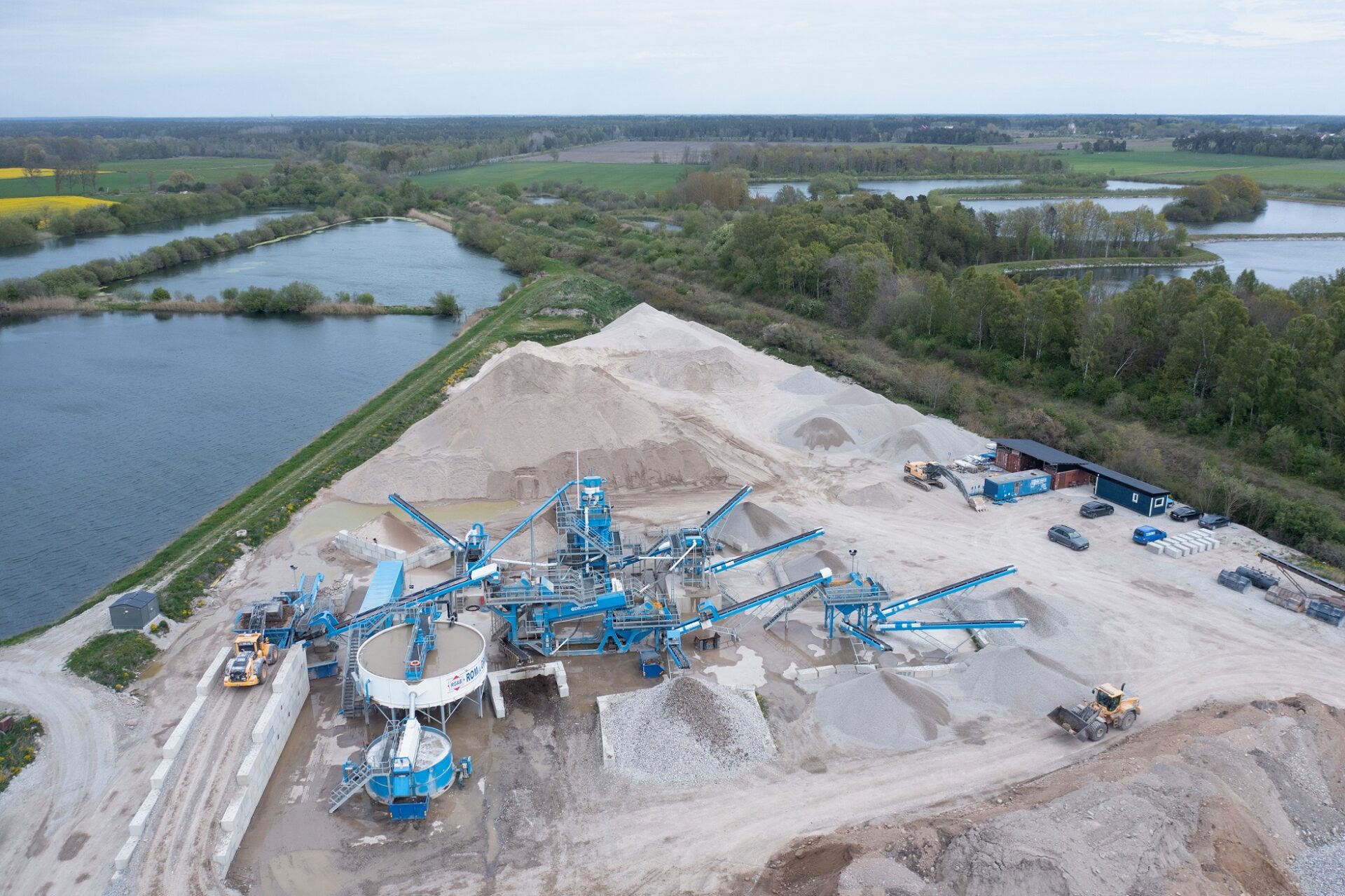 Aerial photograph of Roma Grus’s CDE recycling facility on Gotland, showing conveyor systems, washing units, and stockpiles of recycled aggregates near water bodies and green fields.