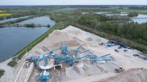 Aerial photograph of Roma Grus’s CDE recycling facility on Gotland, showing conveyor systems, washing units, and stockpiles of recycled aggregates near water bodies and green fields.