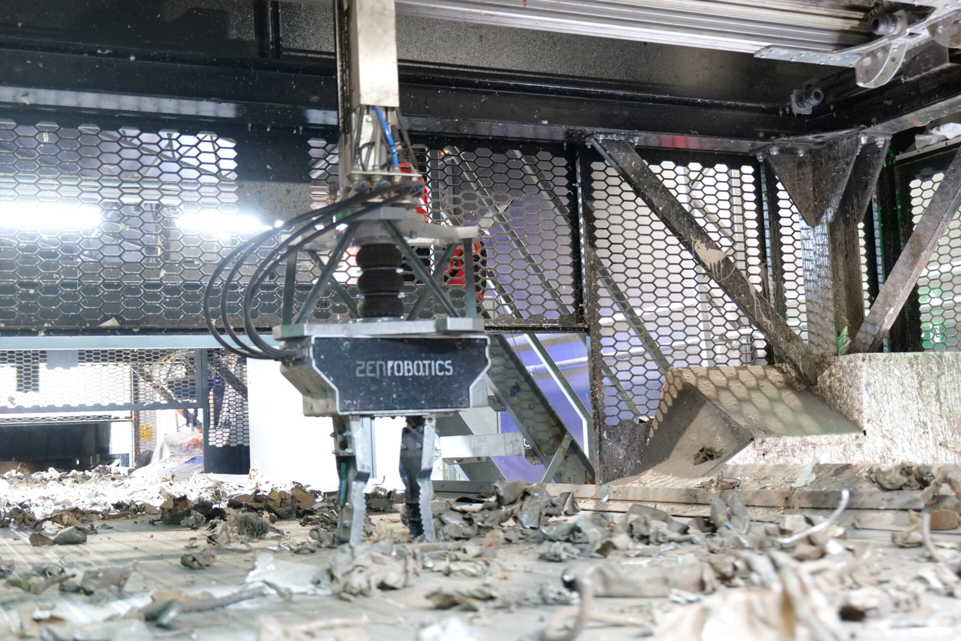 Close-up of a Zen Robotics Heavy Picker robotic arm with gripper, sorting pieces of scrap metal on a conveyor belt inside a recycling facility.