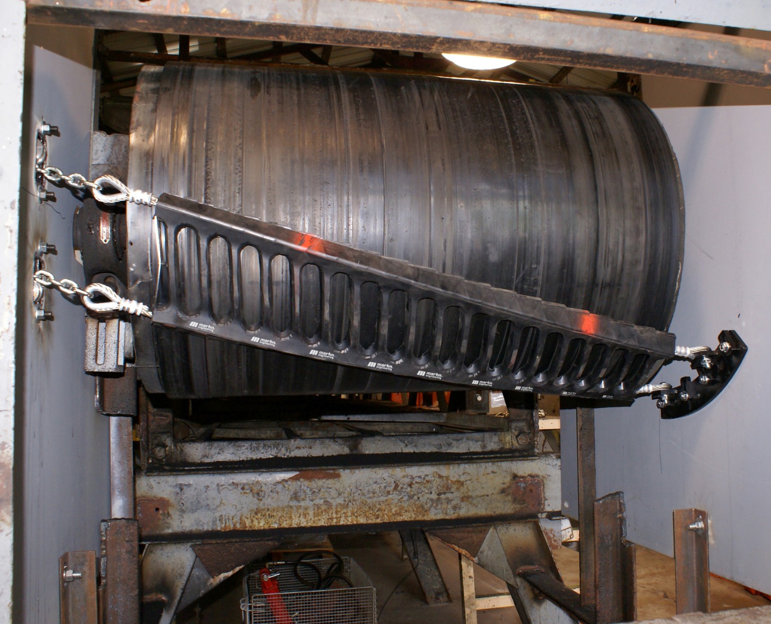 Close-up of a conveyor head pulley with a Martin Engineering cleaning blade installed, showing the tensioning system and mounting setup.